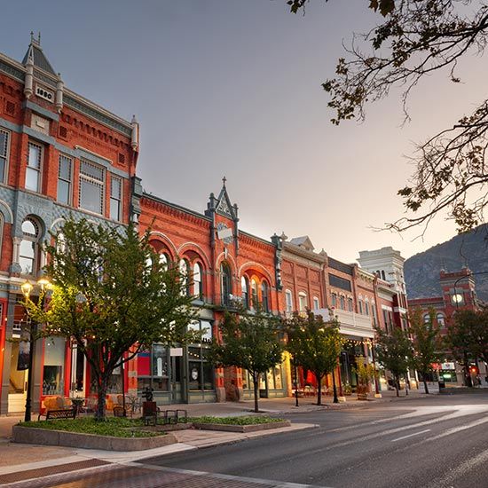 Associate Members; Historic street at dawn with red-brick Victorian buildings, illuminated shops, and tree-lined sidewalks, evoking a calm and nostalgic atmosphere.